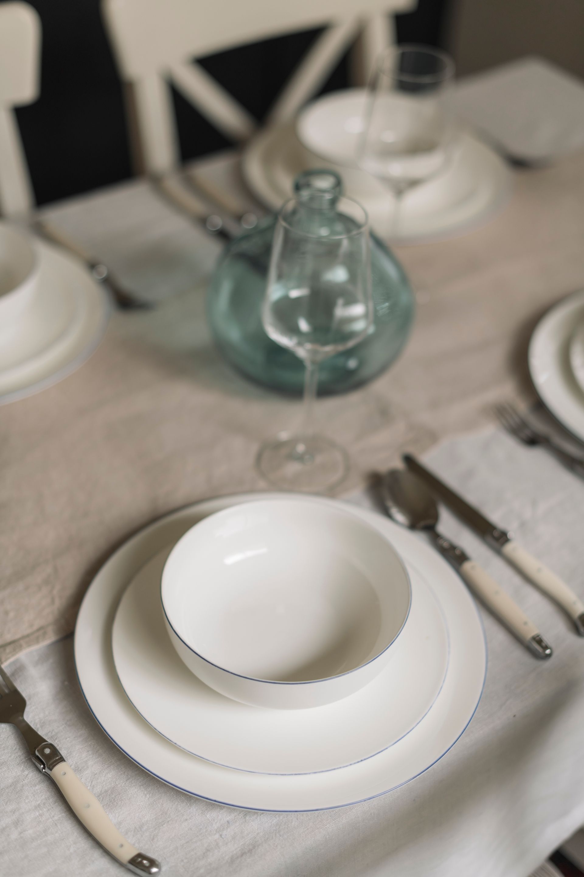 A table set with white plates , bowls , silverware and a vase.