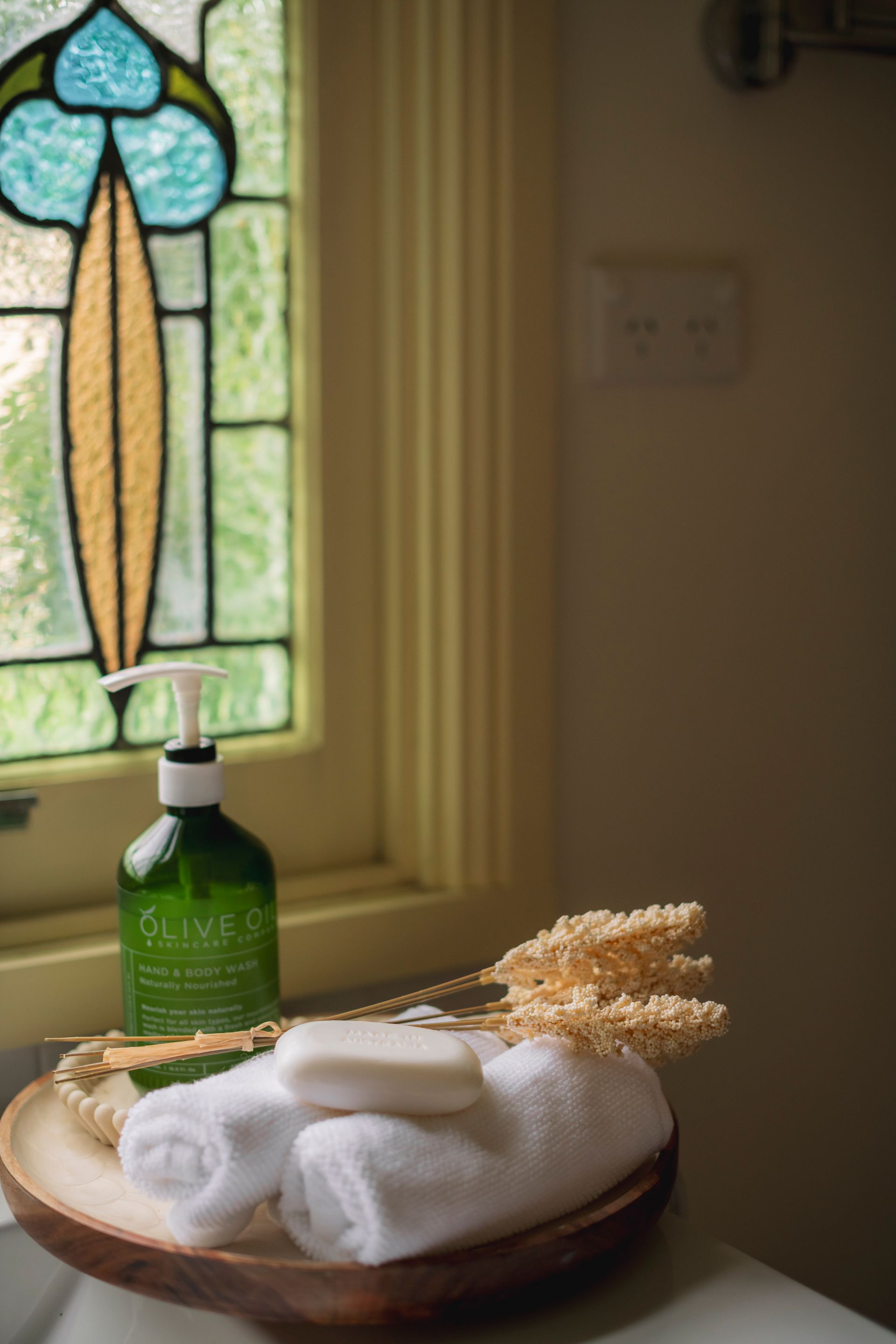 A bowl of towels , soap , and a stained glass window in a bathroom.