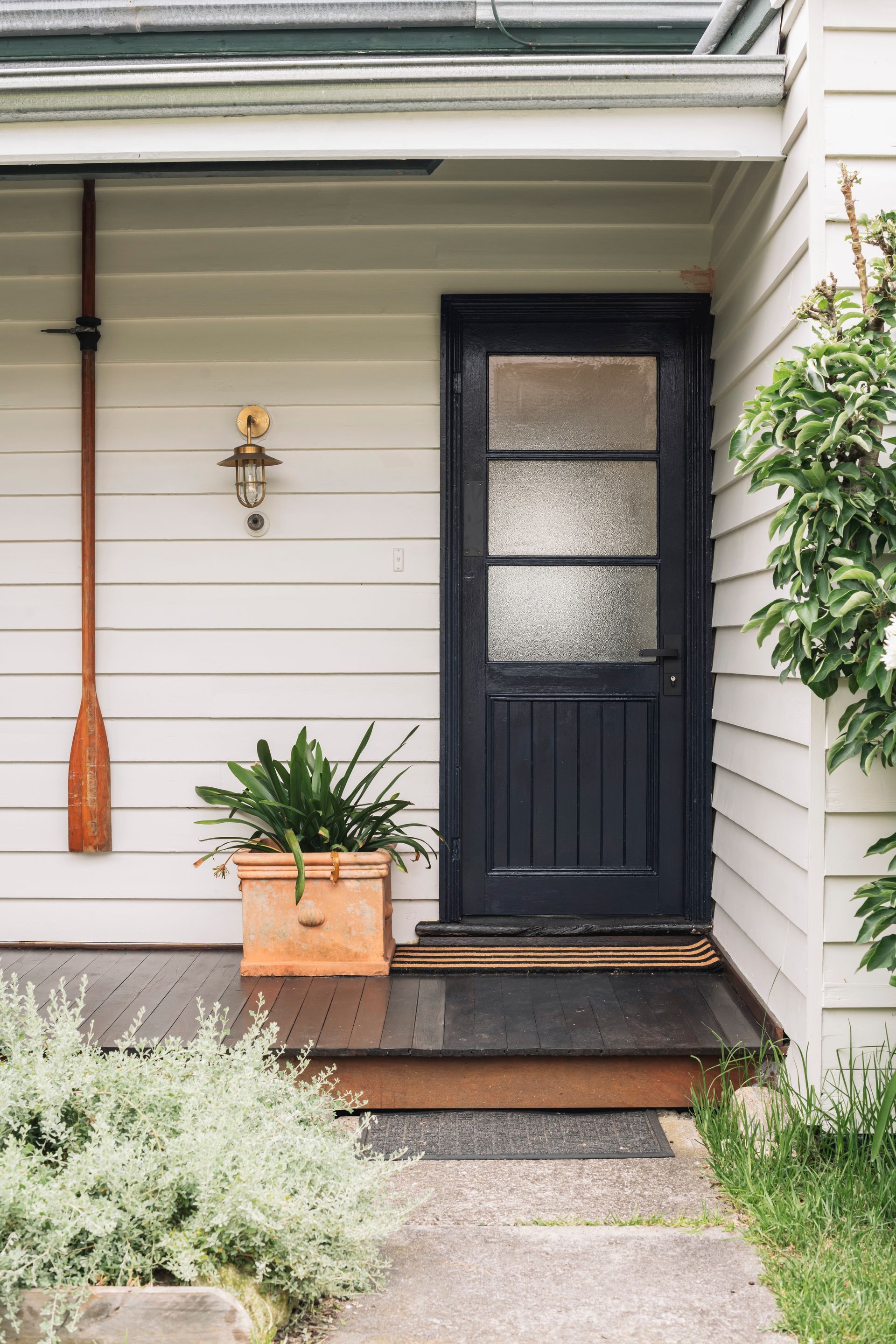 A white house with a black door and a potted plant on the porch.