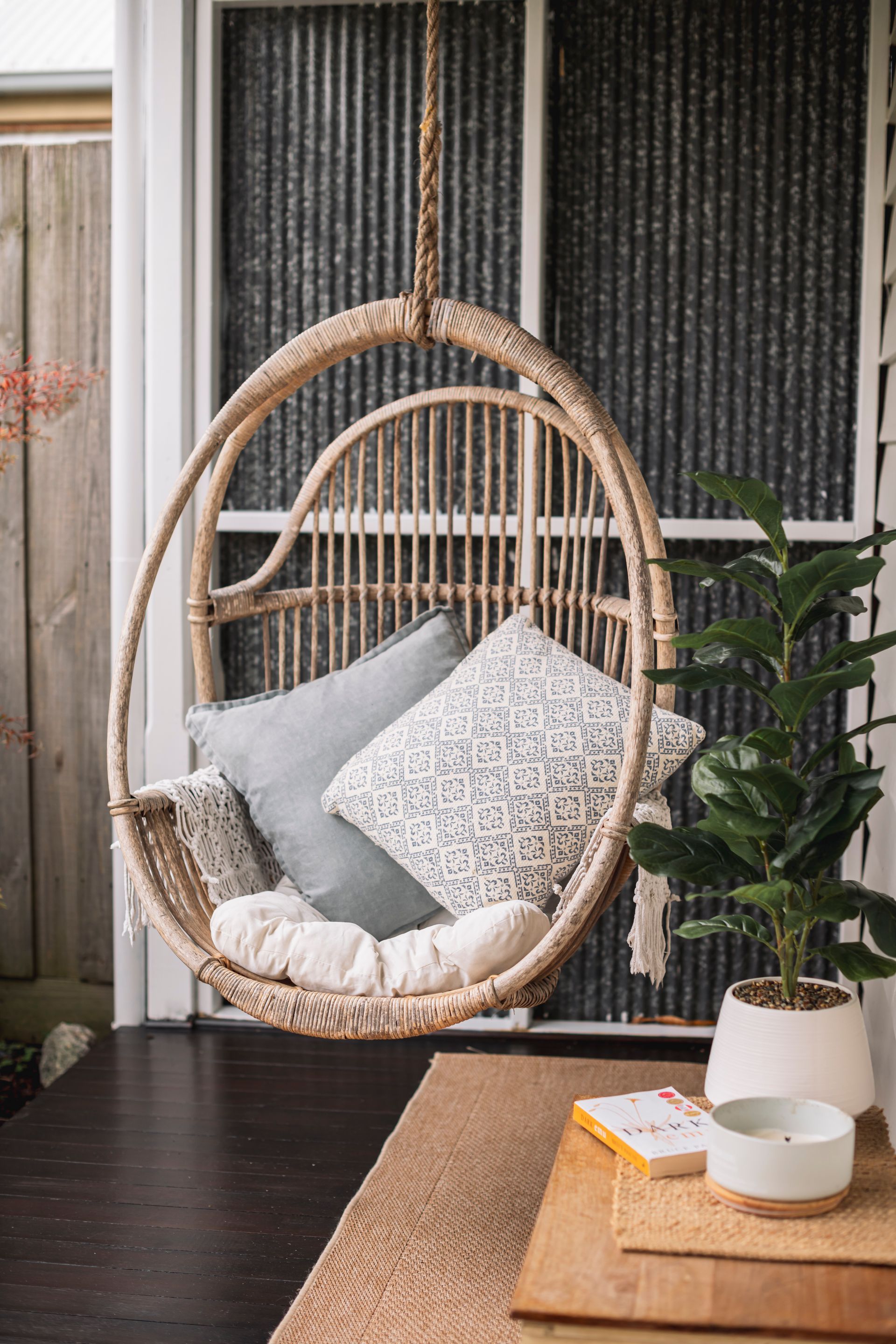 A hanging chair with pillows and a plant on a porch.