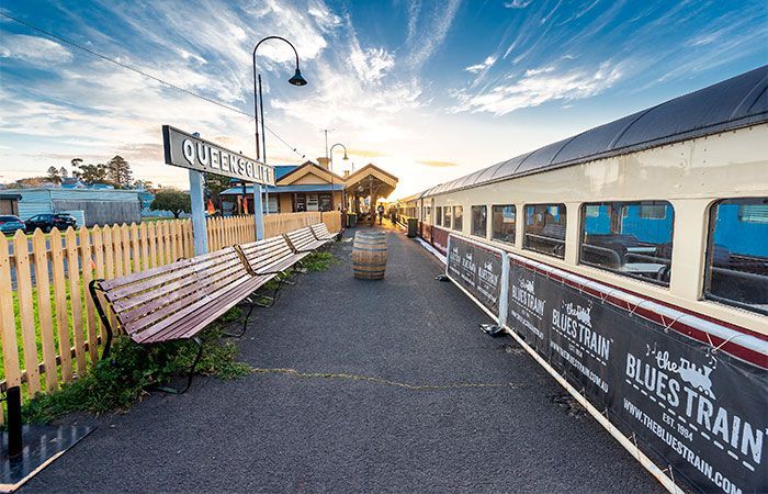 A train is pulling into a train station with a wooden bench in the foreground. Blues Train 