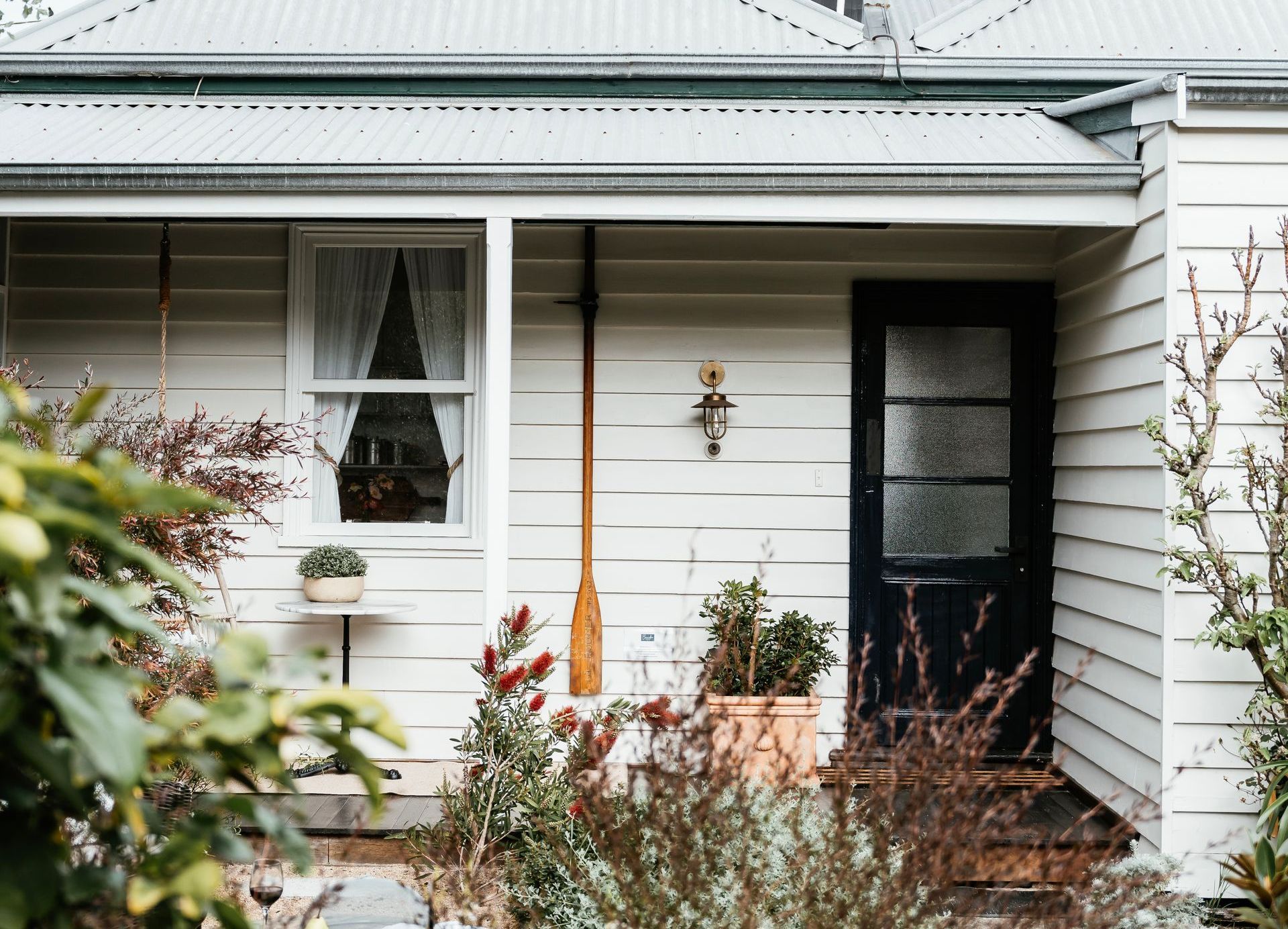 A white house with a Navy Blue door and a white bench on the porch.