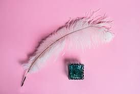 A white feather and a green stone on a pink background.