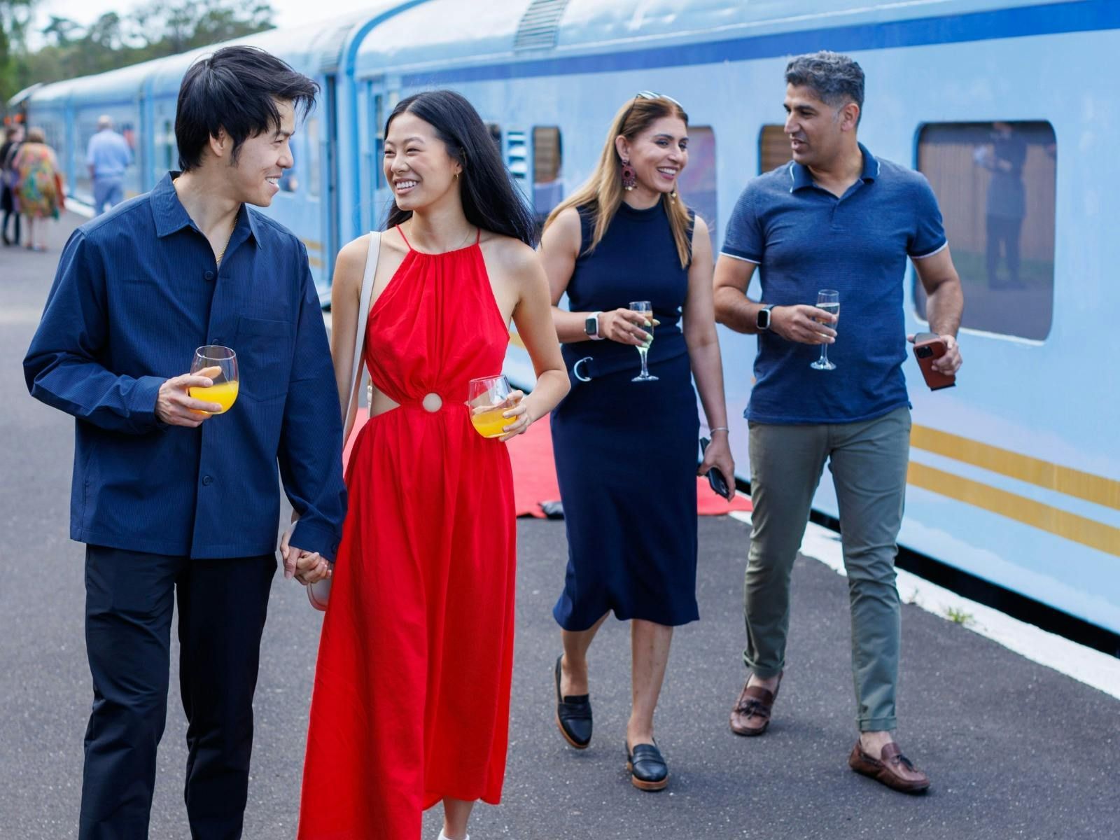 A group of people are standing next to a train holding hands and drinking wine. Qtrain 