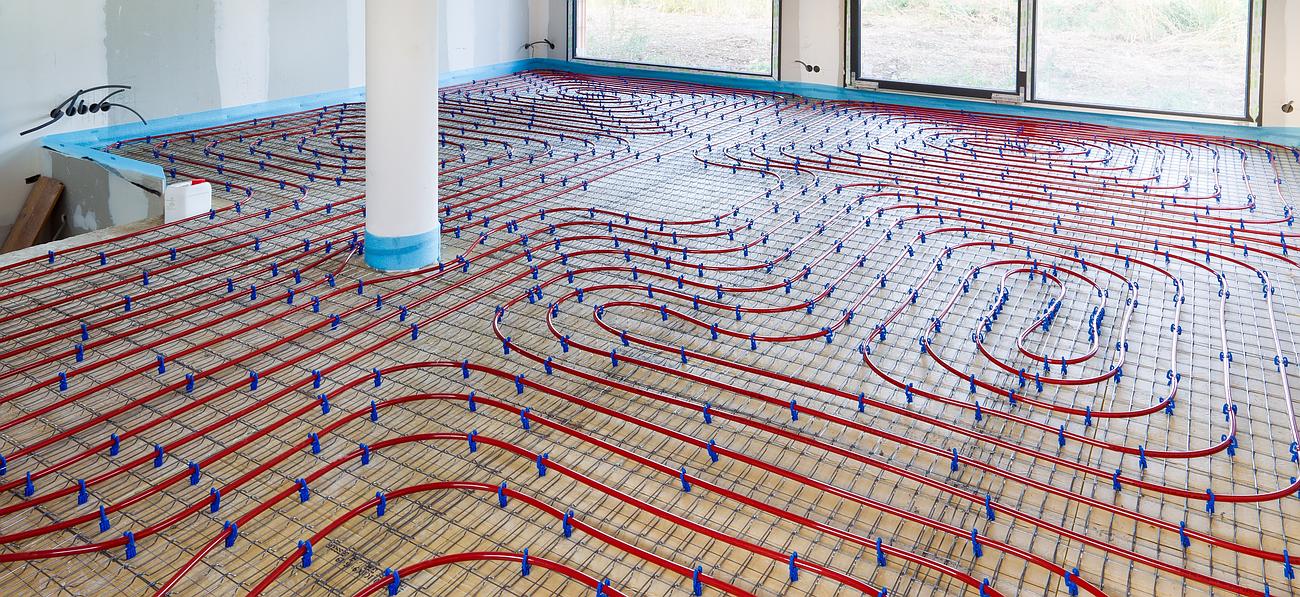 Installation d'un système de chauffage au sol radiant avec des tubes rouges, fixés par des clips bleus, sur un sous-plancher.