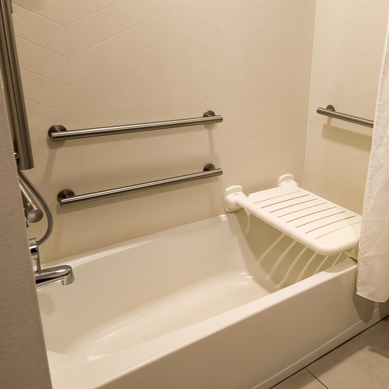 Baignoire équipée de barres d’appui murales en métal et d’un siège de douche rabattable pour salle de bain accessible