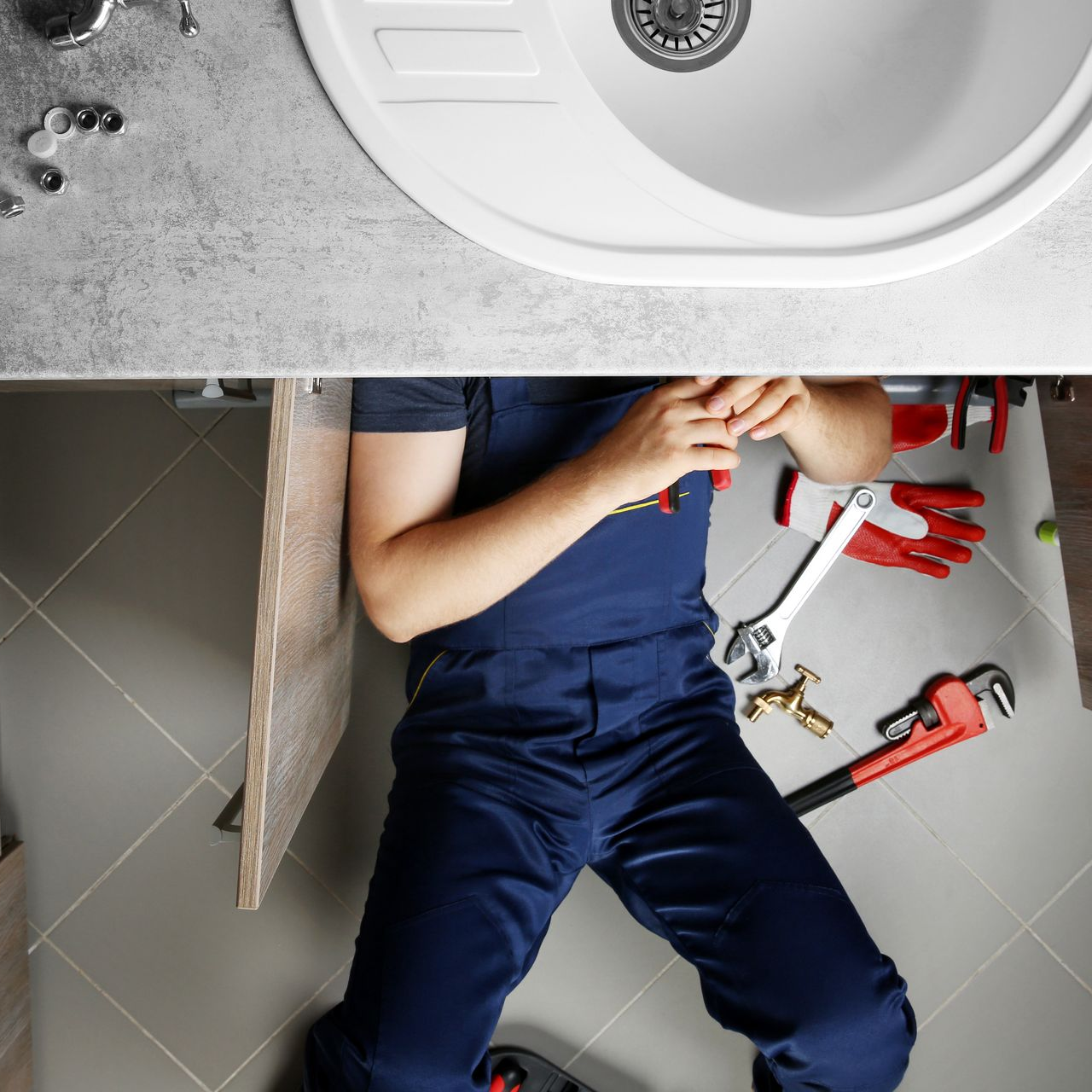 Plombier allongé sous un lavabo, en train de travailler avec des outils de plomberie posés au sol