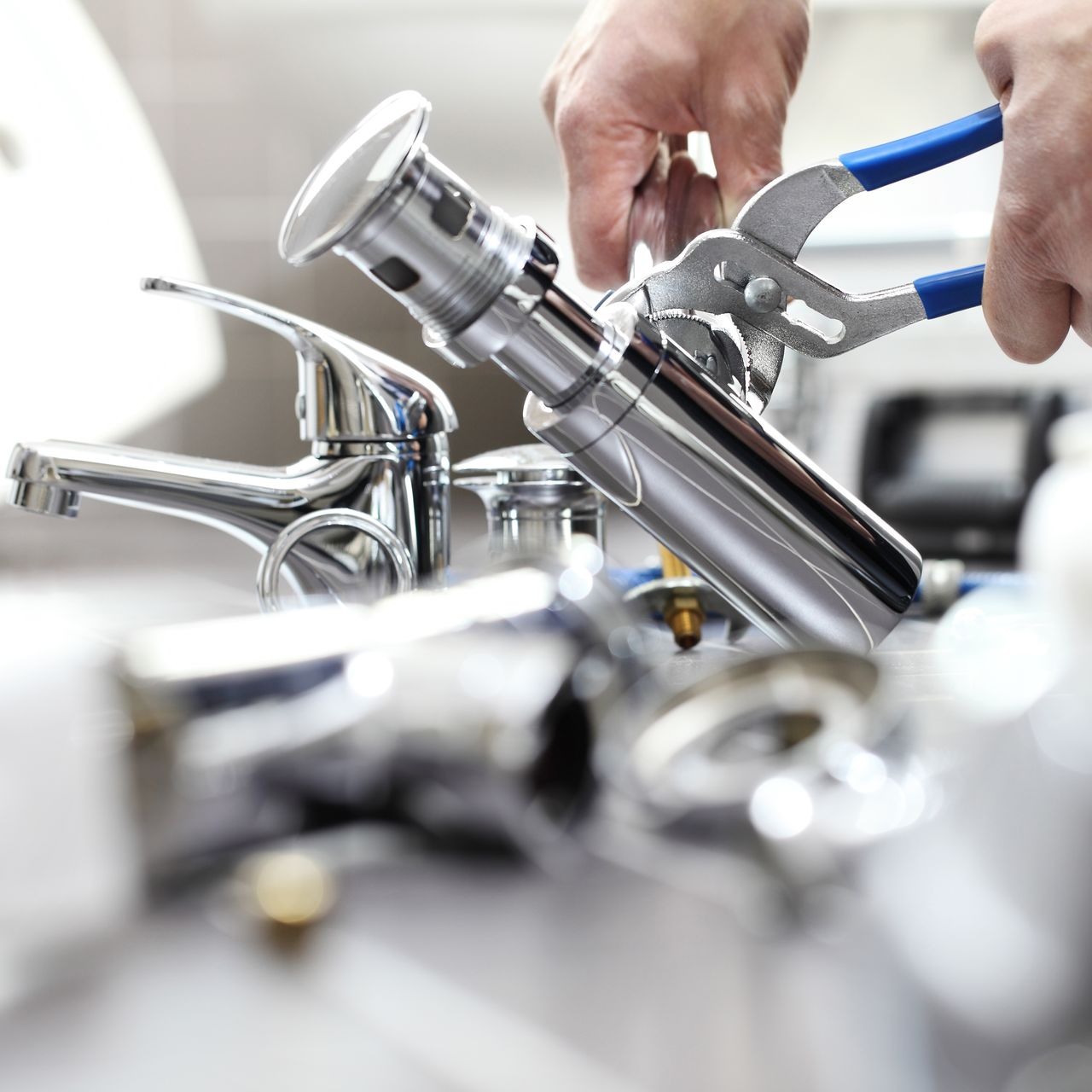 Mains utilisant une pince pour serrer un siphon chromé sur un plan de travail, avec des pièces de robinetterie en arrière-plan