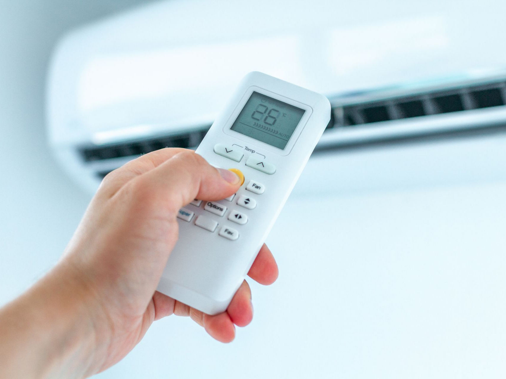 Main tenant une télécommande affichant 26 °C devant un climatiseur mural