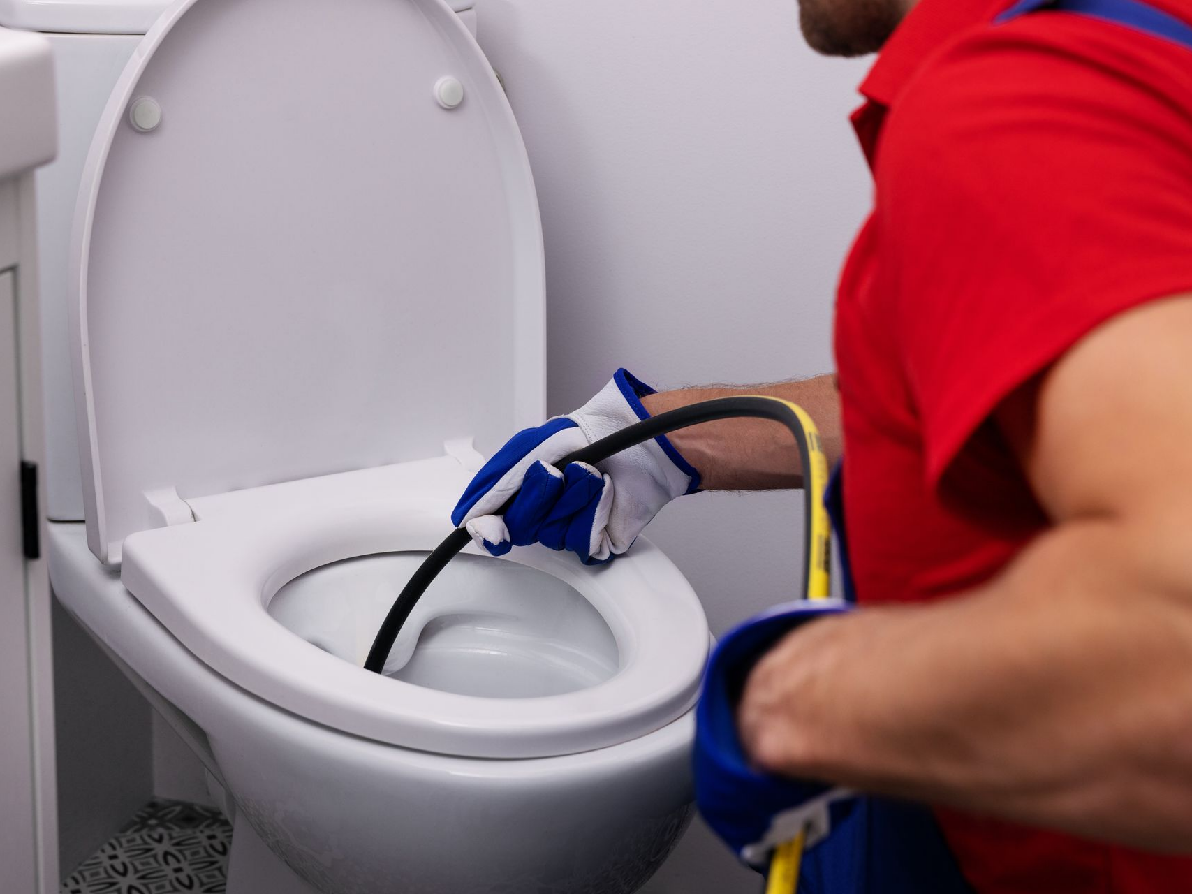 Personne portant des gants et utilisant un furet pour déboucher une cuvette de toilettes