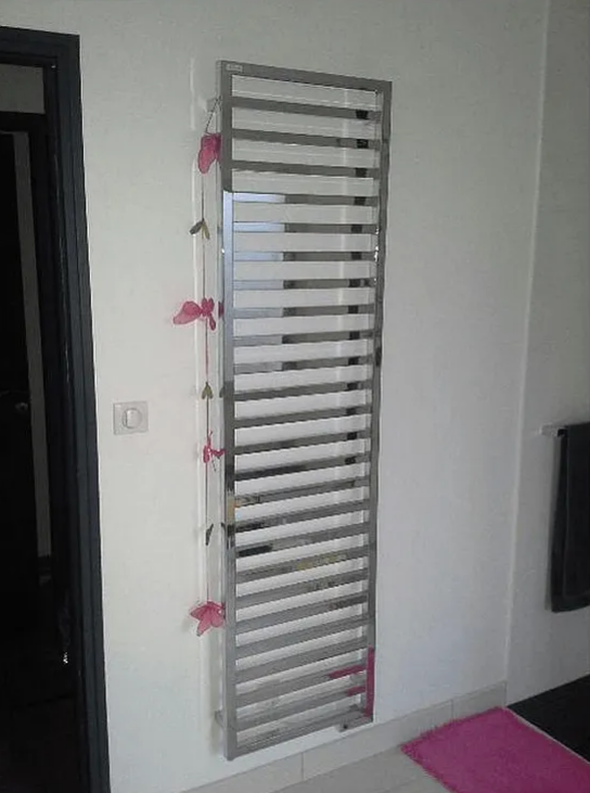 Sèche-serviettes en acier inoxydable sur un mur blanc, touches de rose, près d'une porte et d'une télévision.