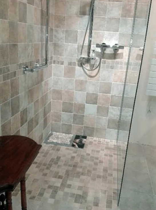 Cabine de douche avec carrelage carré beige et marron, porte en verre et sol en galets.