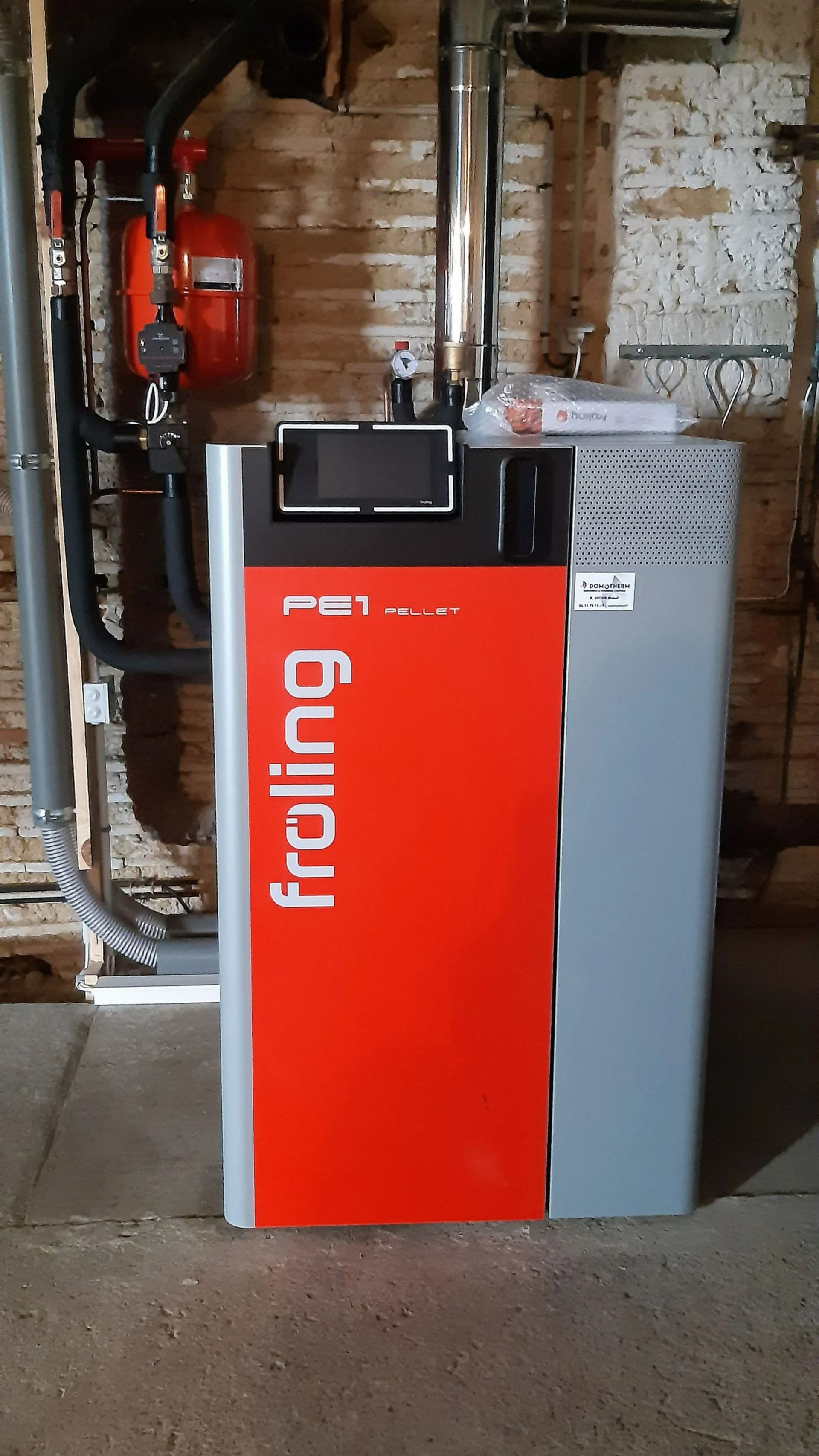 Un système de chauffage rouge et gris portant l'inscription fröling se trouve dans un sous-sol.