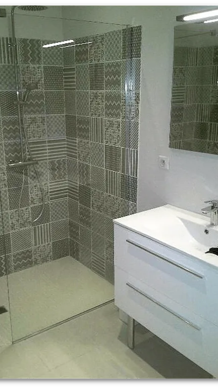 Salle de bains moderne avec paroi de douche grise à motifs, porte en verre, meuble-lavabo blanc et miroir.