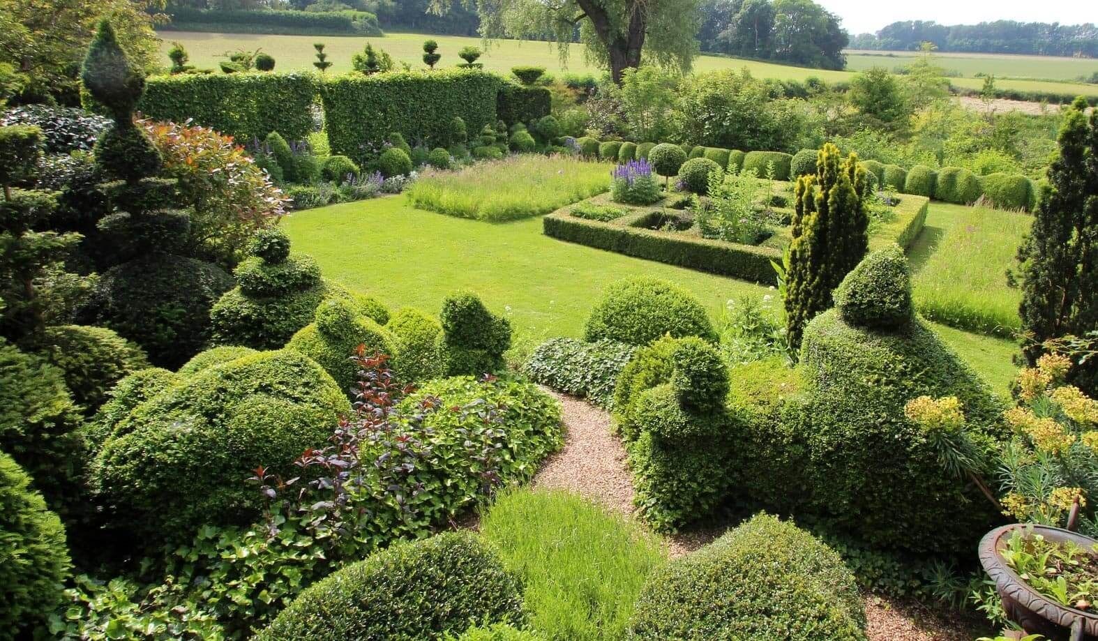 Formaler Garten mit geschnittenen Büschen, Rasenflächen und Wegen in sonniger Lage im Freien.