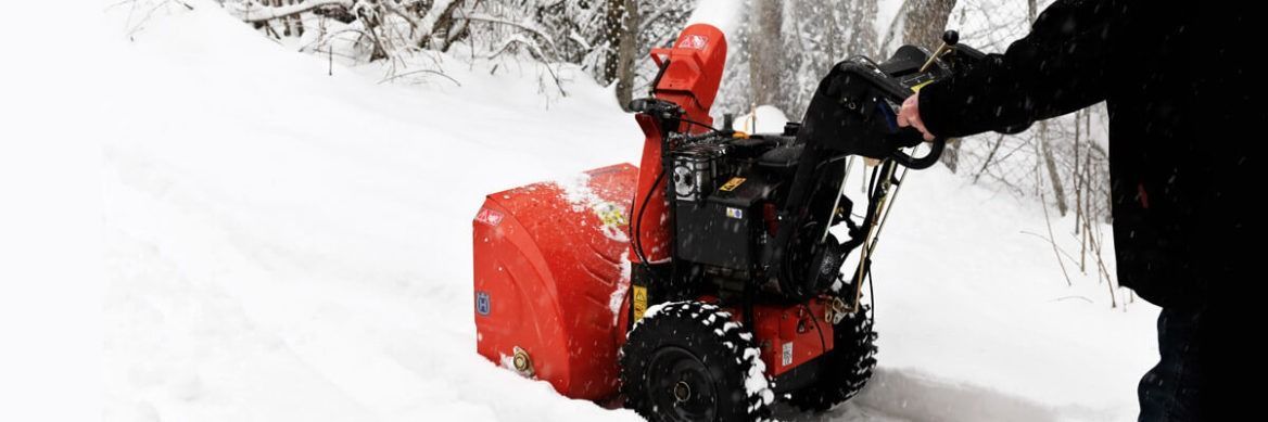 Eine Person benutzt eine rote Schneefräse auf einem schneebedeckten Weg.