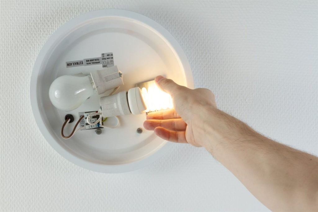 Handwechsel einer leuchtenden Glühbirne in einer weissen Deckenleuchte.