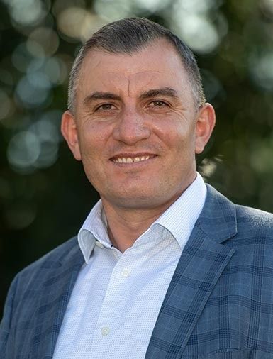 Ein Mann in blau-karierter Jacke und weissem Hemd lächelt im Freien.