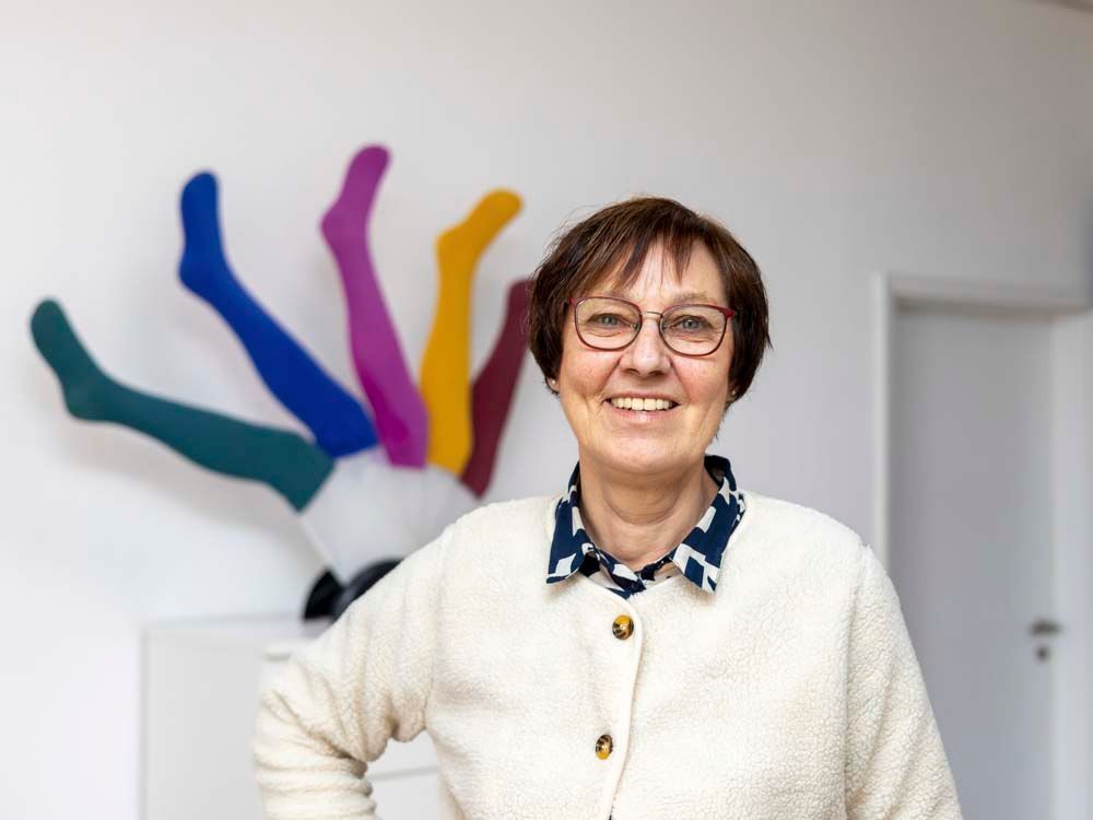 Eine Frau in einem rosa Pullover und Schal lächelt in die Kamera.