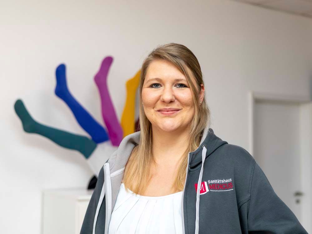 Eine Frau in einem roten Hemd steht vor einer Kommode . Im Hintergrund sind Beinprothesen zu sehen.