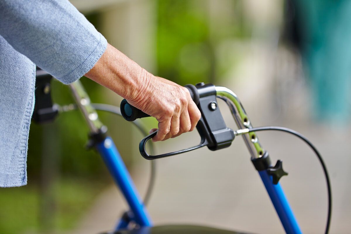 Eine ältere Frau benutzt einen Rollator auf einem Bürgersteig.