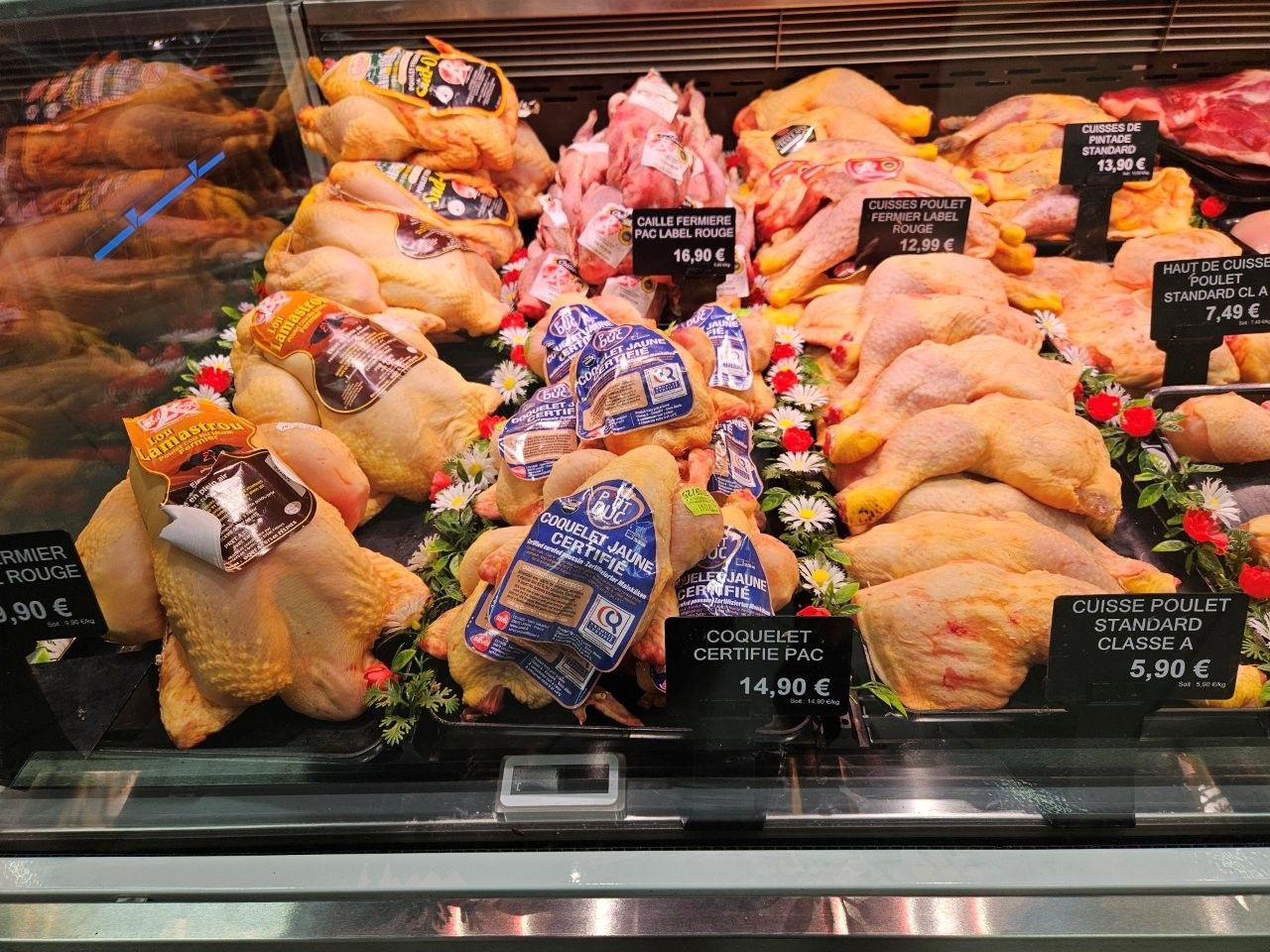 Eine Kühlvitrine mit rohem Hühnerfleisch, versehen mit Preisschildern, in einem Markt.