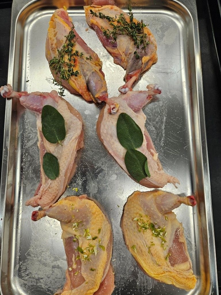 Rohe Wachtelstücke, mit Kräutern gewürzt, auf einem Metalltablett.