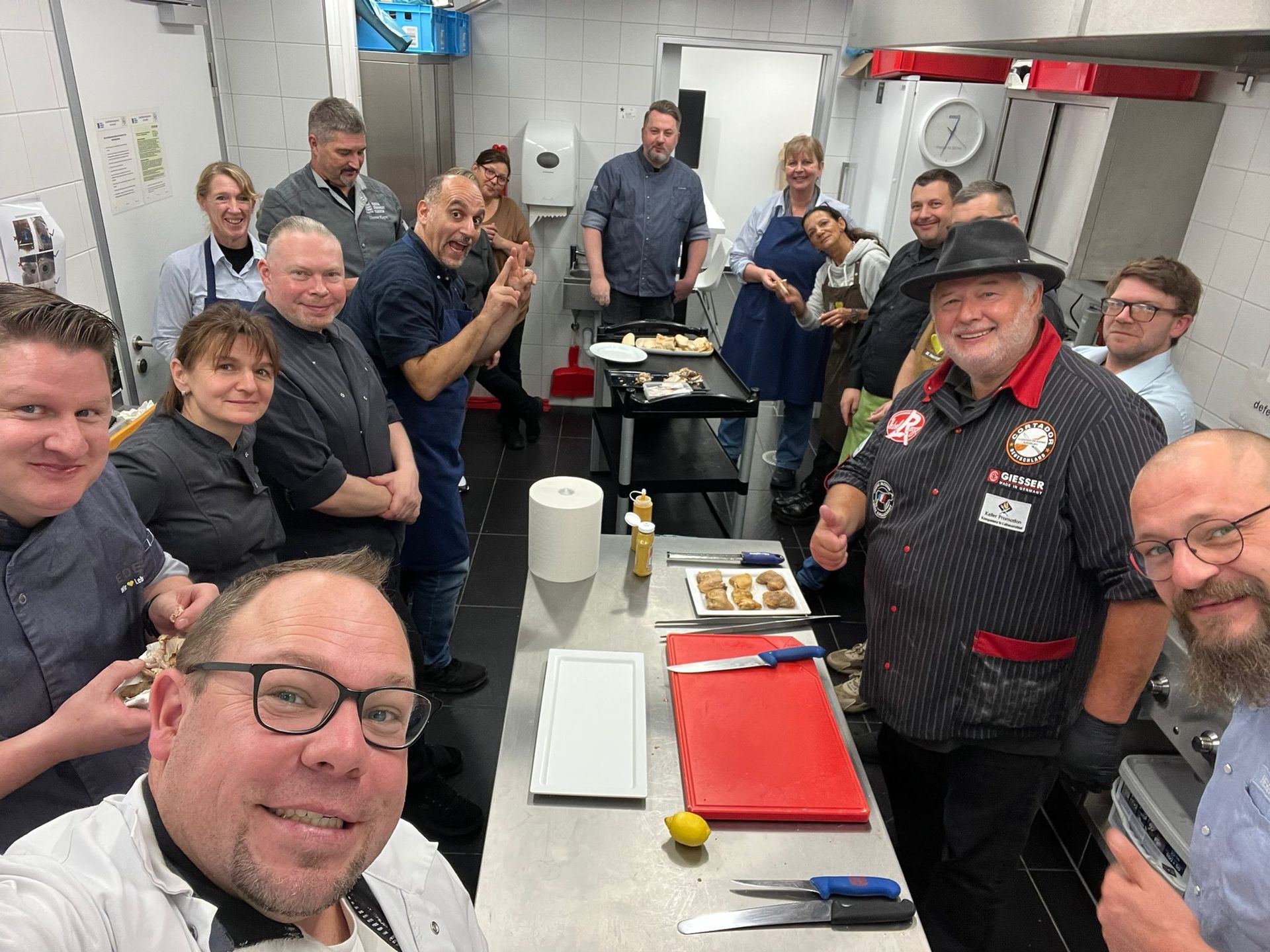 Eine Gruppe von Köchen in einer Küche, die in die Kamera lächeln. Einige zeigen den Daumen nach oben.