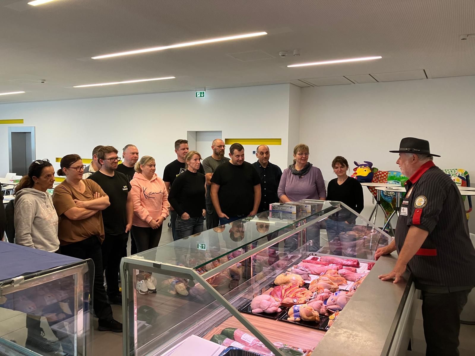 Metzger demonstriert einer Gruppe in einem hell erleuchteten Laden Fleischzuschnitte.