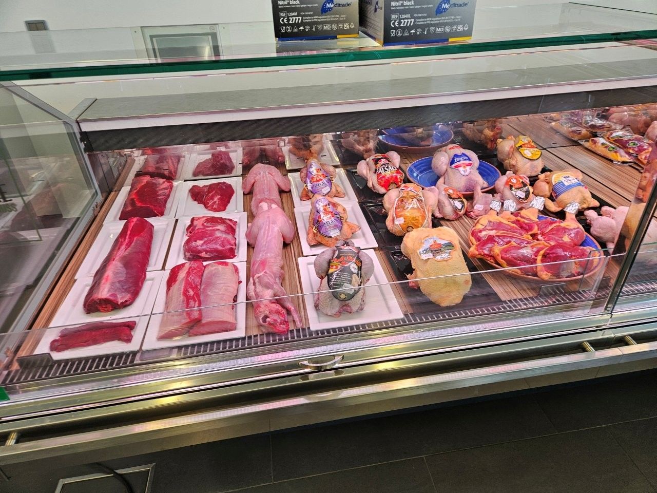 Fleischauslage in einem Geschäft. Verschiedene Stücke von rotem Fleisch und Geflügel werden unter heller Beleuchtung präsentiert.