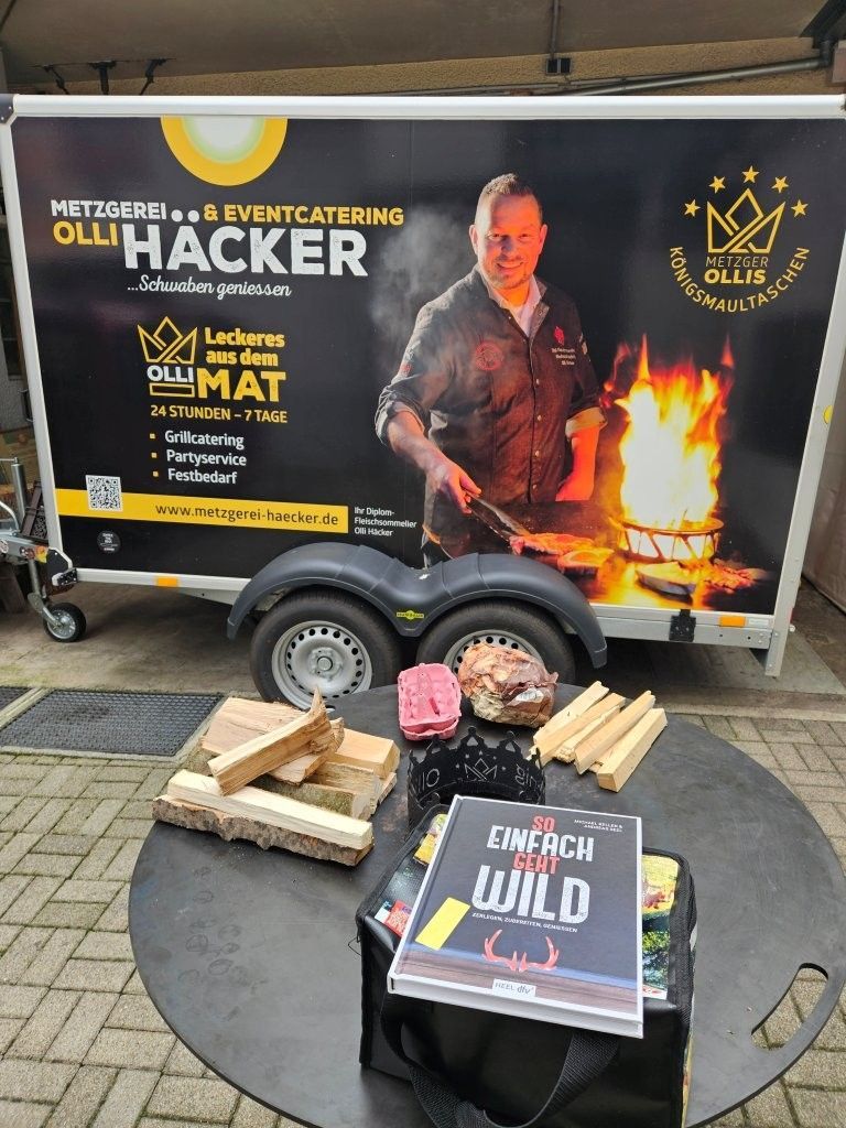 Food-Catering-Anhänger mit Grill, Brennholz, Lebensmitteln und Buch „Einfach Wild“.
