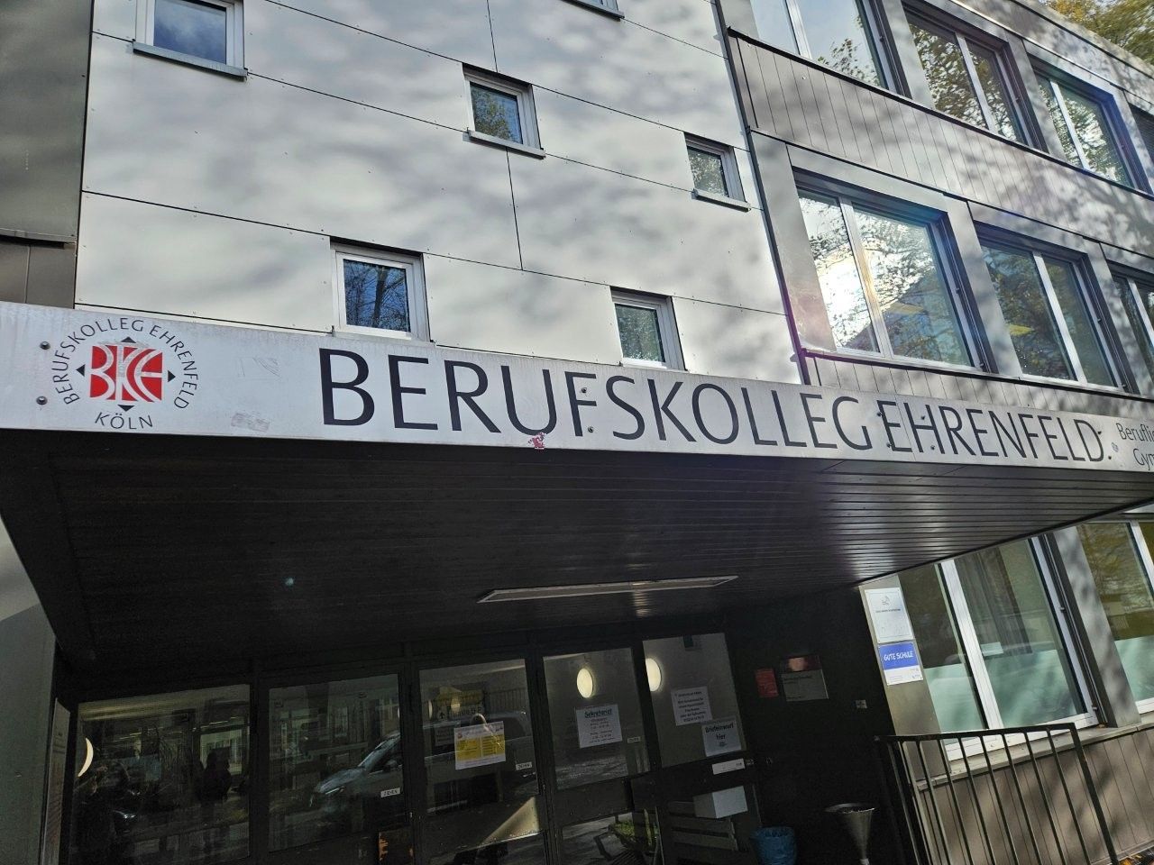 Gebäude des BERUFSKOLLEG EHRENFELD mit Schild über dem Eingang. Weiß-graue Fassade, mehrere Fenster.