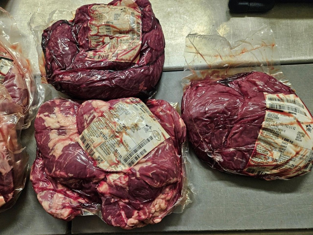 Vakuumverpackte Packungen mit rotem Fleisch auf einer Metalloberfläche. Jede Packung ist etikettiert.