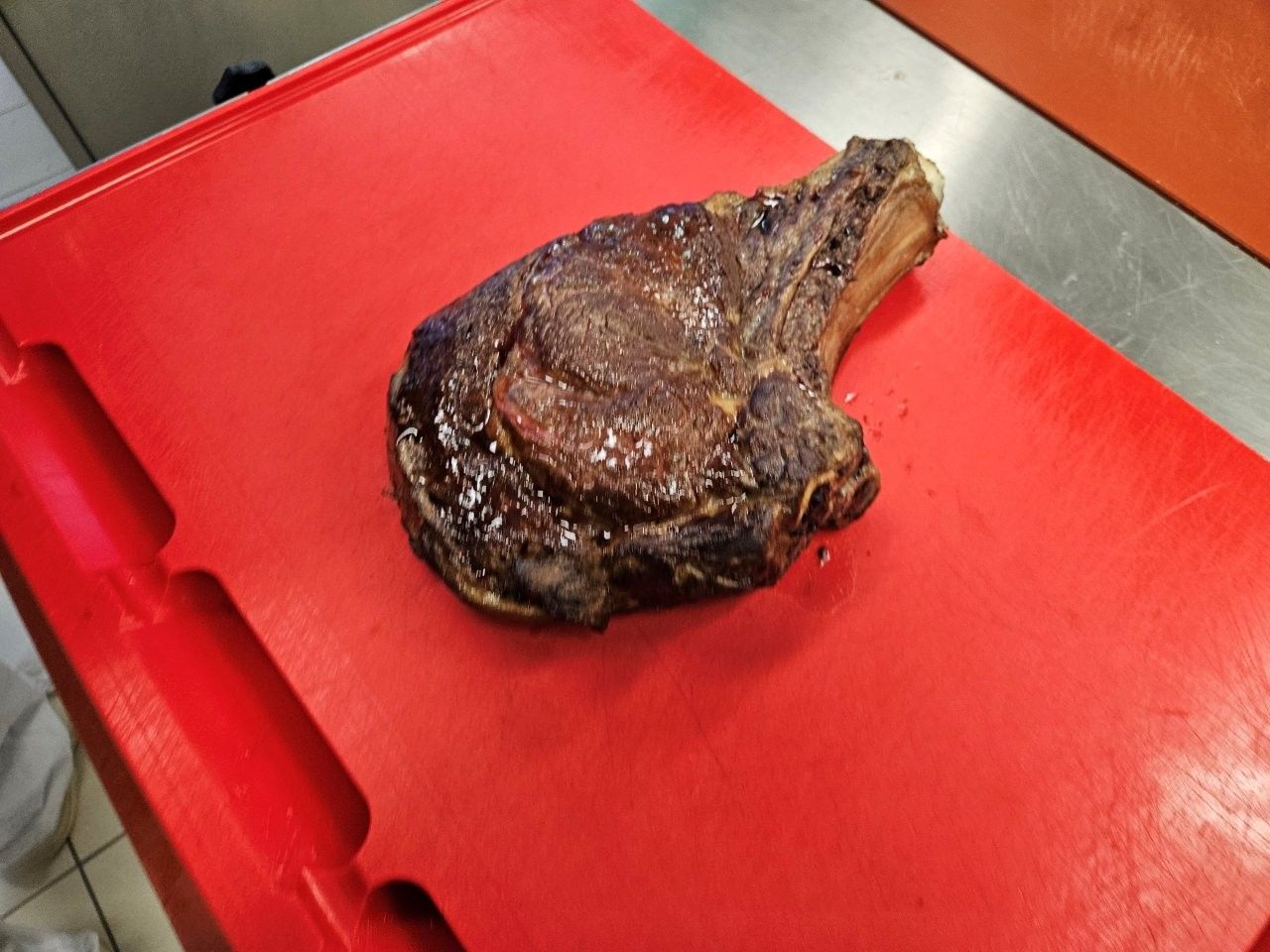 Ein großes, gegartes Ribeye-Steak liegt auf einem roten Schneidebrett und ist bereit zum Aufschneiden.
