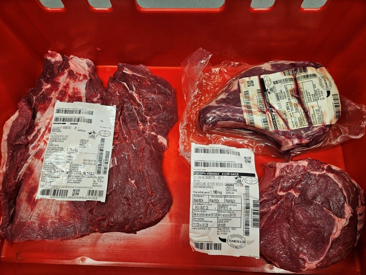 Rohe Rindfleischstücke in einem roten Behälter, mit Preisschildern versehen.