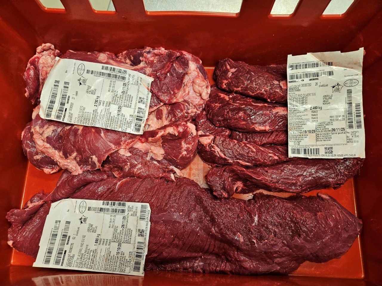 Rohe Rindfleischstücke mit Preisschildern in einem roten Behälter.