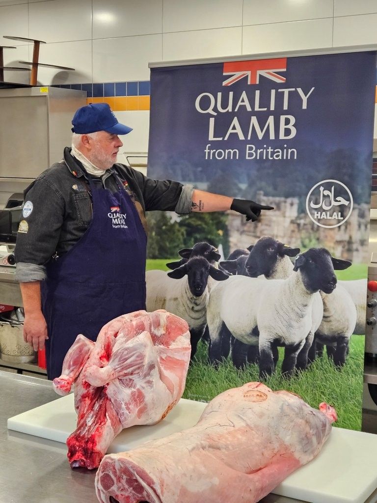 Ein Mann zeigt auf ein Schild mit der Aufschrift „Qualitätslamm aus Großbritannien“, auf dem zwei Stücke rohes Lammfleisch abgebildet sind.
