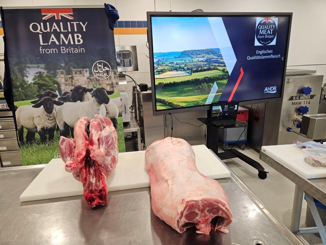 Zerlegte Lammfleischstücke auf einem Edelstahltisch, im Hintergrund ein Werbebanner.
