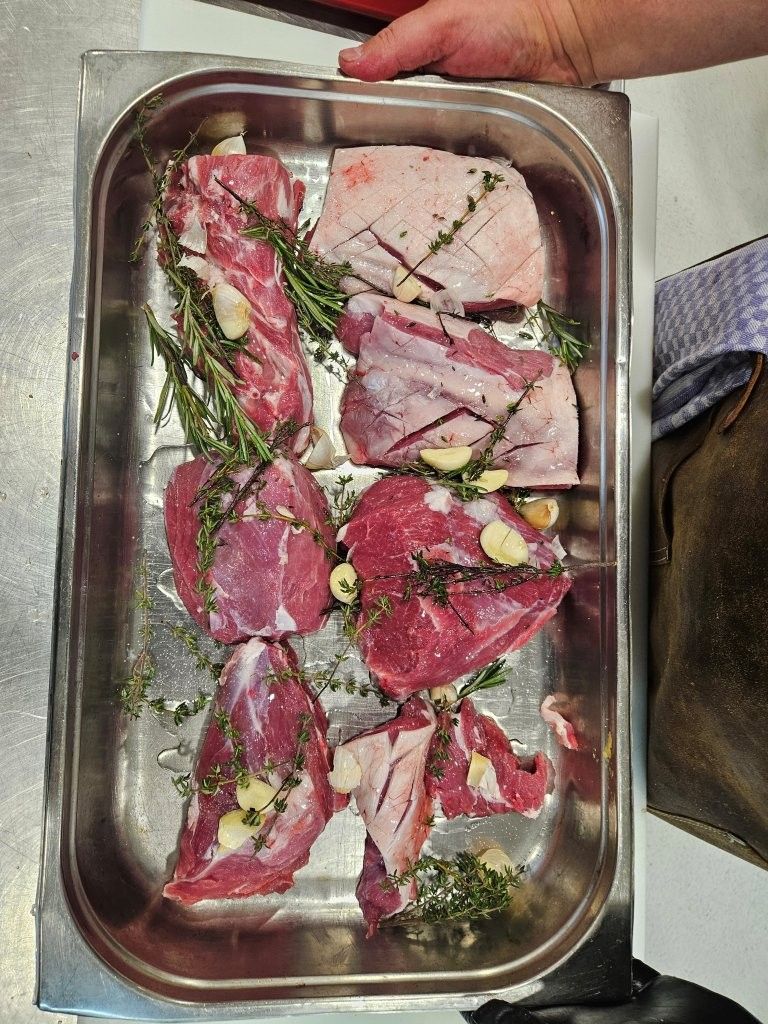 Rohe Fleischstücke mit Kräutern und Knoblauch in einer Metallschale, bereit zum Kochen.