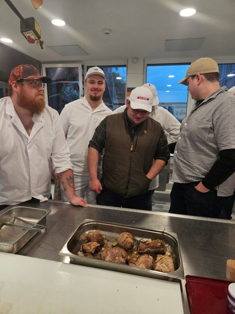 Fünf Männer begutachten in einer Großküche einen Topf mit gekochtem Essen. Einer von ihnen, der eine Weste trägt, steht in der Mitte.
Feedback