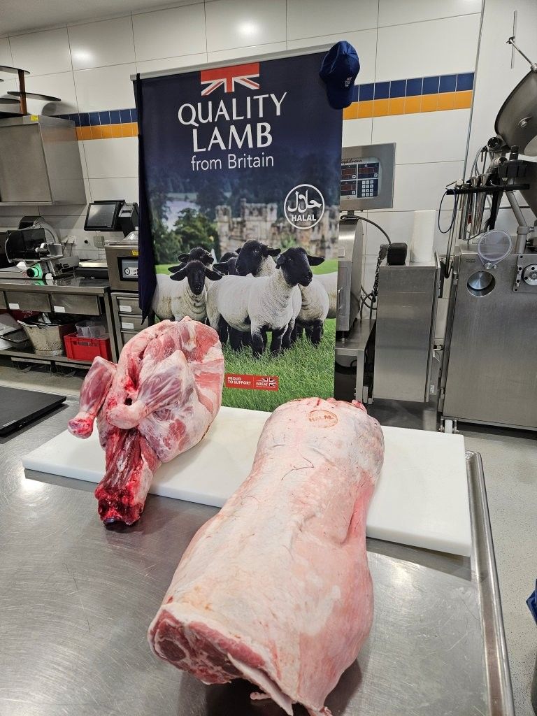 Rohe Lammfleischstücke liegen auf einer Edelstahltheke neben einem Banner mit der Aufschrift „Qualitätslamm aus Großbritannien“. Küchenszene.