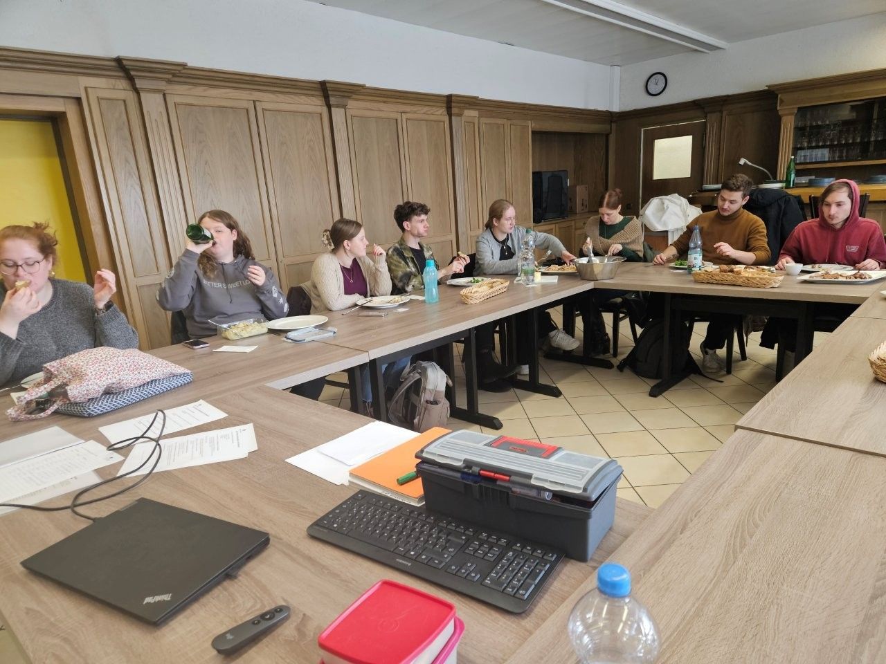 Eine Gruppe von Menschen sitzt in einem Raum um einen Tisch und isst.