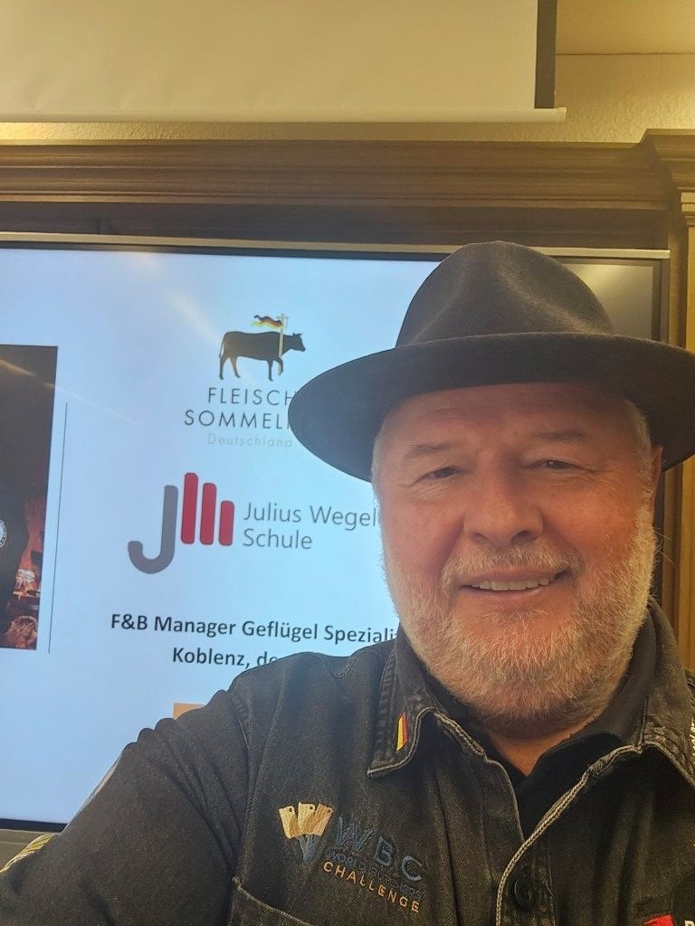 Ein Mann mit Hut lächelt vor einem Bildschirm mit Logo und Text.