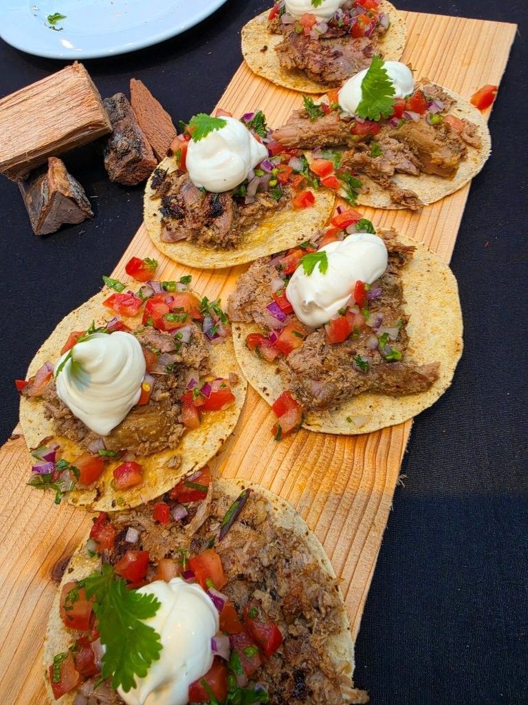 Assorted tacos topped with sour cream, salsa, and cilantro on a wooden serving board