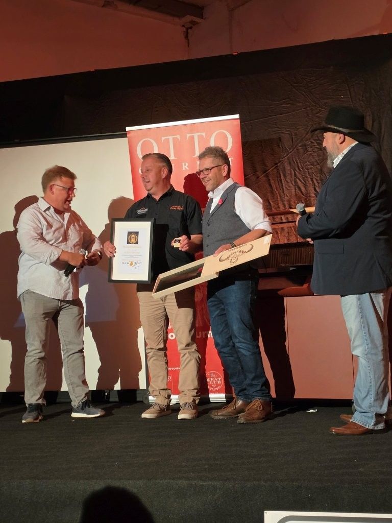 Four men onstage at an award presentation, holding a framed certificate and a wooden plaque.