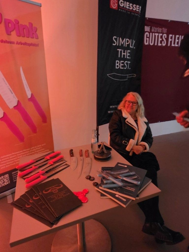 Woman seated at a booth with pink and black brochures and display banners for a trade show