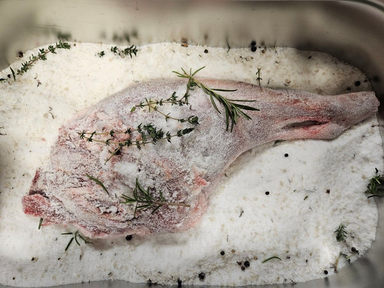 Lammkeule in einer Auflaufform, mit Salz, Kräutern und Pfefferkörnern bestreut.