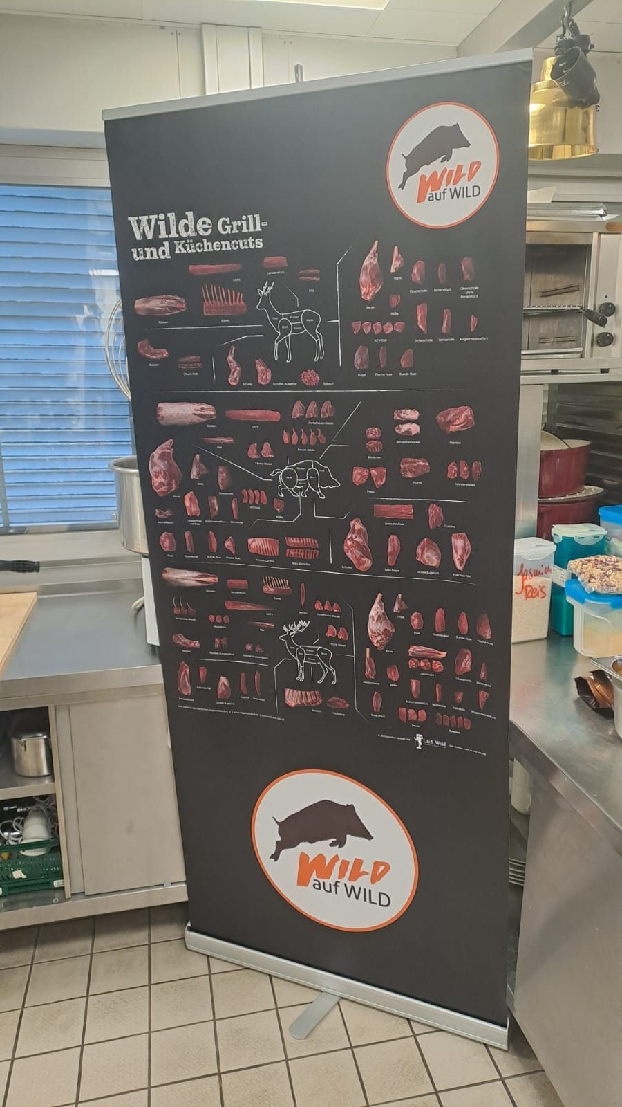 Roll-Up-Banner mit Illustrationen von Fleischzuschnitten, schwarzem Hintergrund und Logo mit einem Wildschwein in einer Küche.