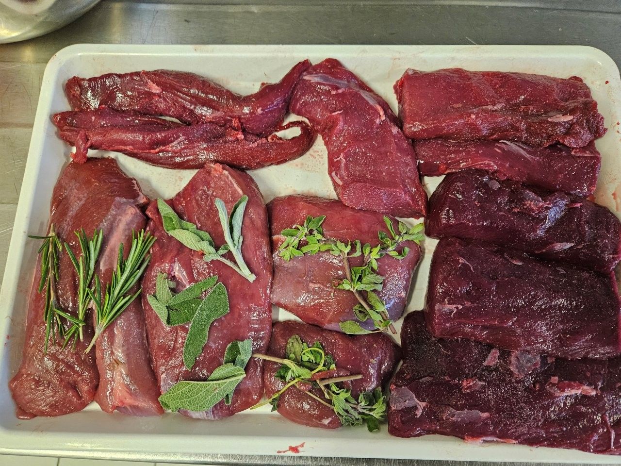 Eine Schale mit rohen, roten Fleischstücken, teilweise mit Kräutern, bereit zum Kochen.