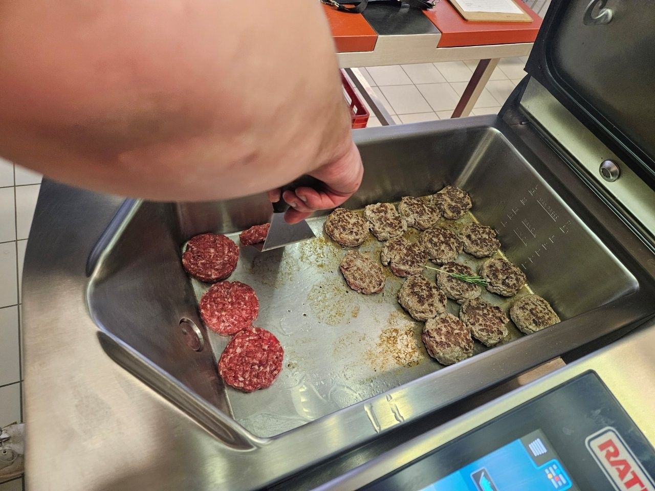 Eine Person grillt Fleischbällchen auf einer Grillplatte. Einige sind roh, andere gar.